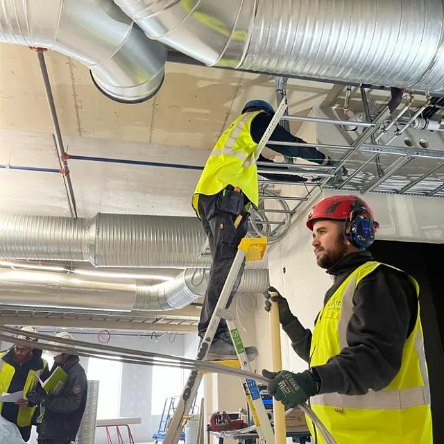 Elektrikere jobber på stige med elektroinstallasjon i industriell setting, installerer elektriske anlegg for industrielt bruk