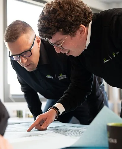 Flere elektrikere diskuterer og ser på blueprint-tegninger i et kontormiljø, planlegger et elektroinstallasjonsprosjekt for nybygg eller rehabilitering