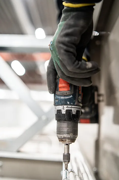 Elektriker bruker drill for å utføre elektroinstallasjon i næringsbygg, installerer elektriske anlegg for effektiv drift