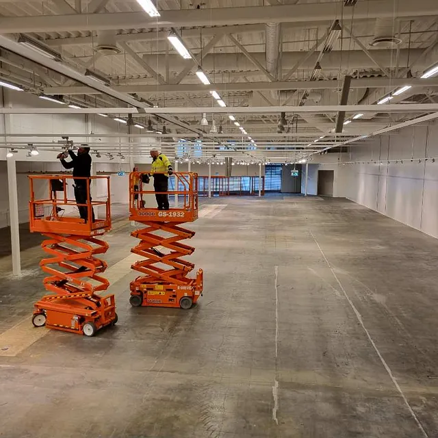 Elektriker bruker sakseheis for å installere lagerbelysning, jobber med elektroinstallasjon i lagerbygning